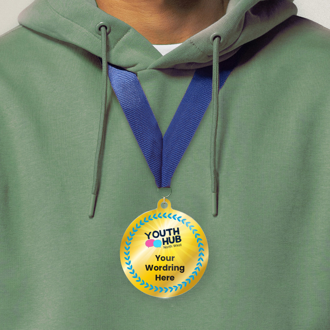 Acrylic personalised medal with blue ribbon showing blue design with blue wreath, Youth Hub logo and personalised wording. Worn around a persons neck wearing a green hoodie.