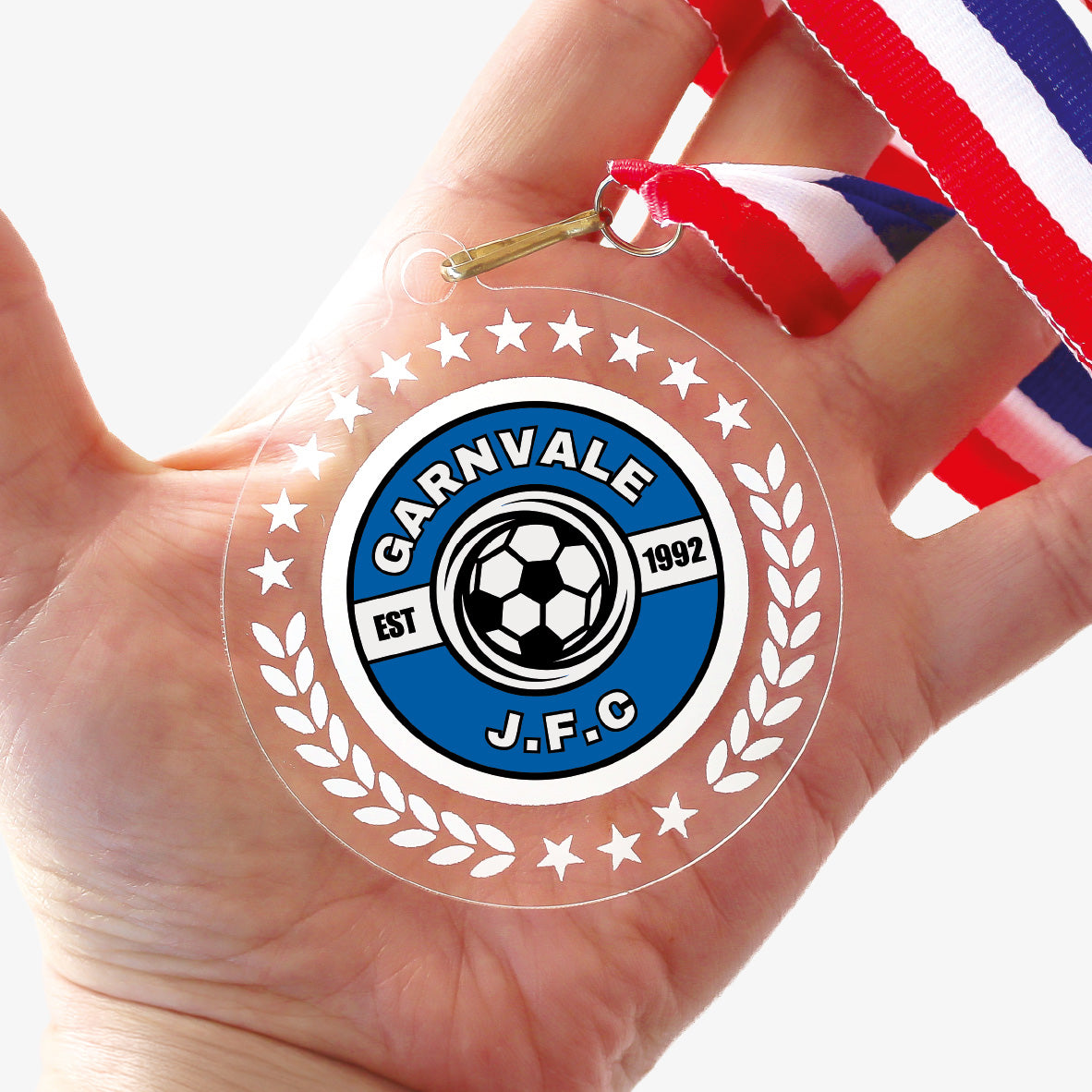 Acrylic personalised medal with stripy ribbon showing clear background with wreath design and 'Garnvale JFC' logo. held in a hand.