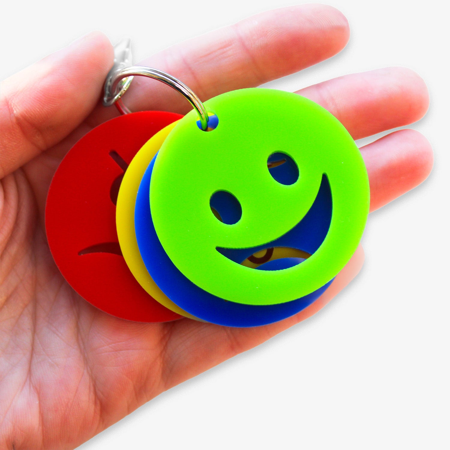 Hand holding keyring with four faces showing different emotions. Green happy face at the front.