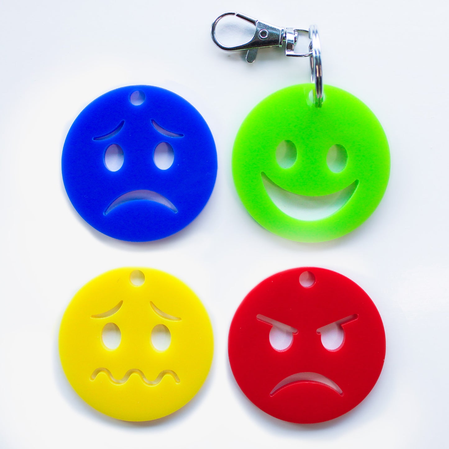 Keyring with four faces showing different emotions. Green happy face on keyring. Blue sad face, yellow confused face, red angry face showed separately.