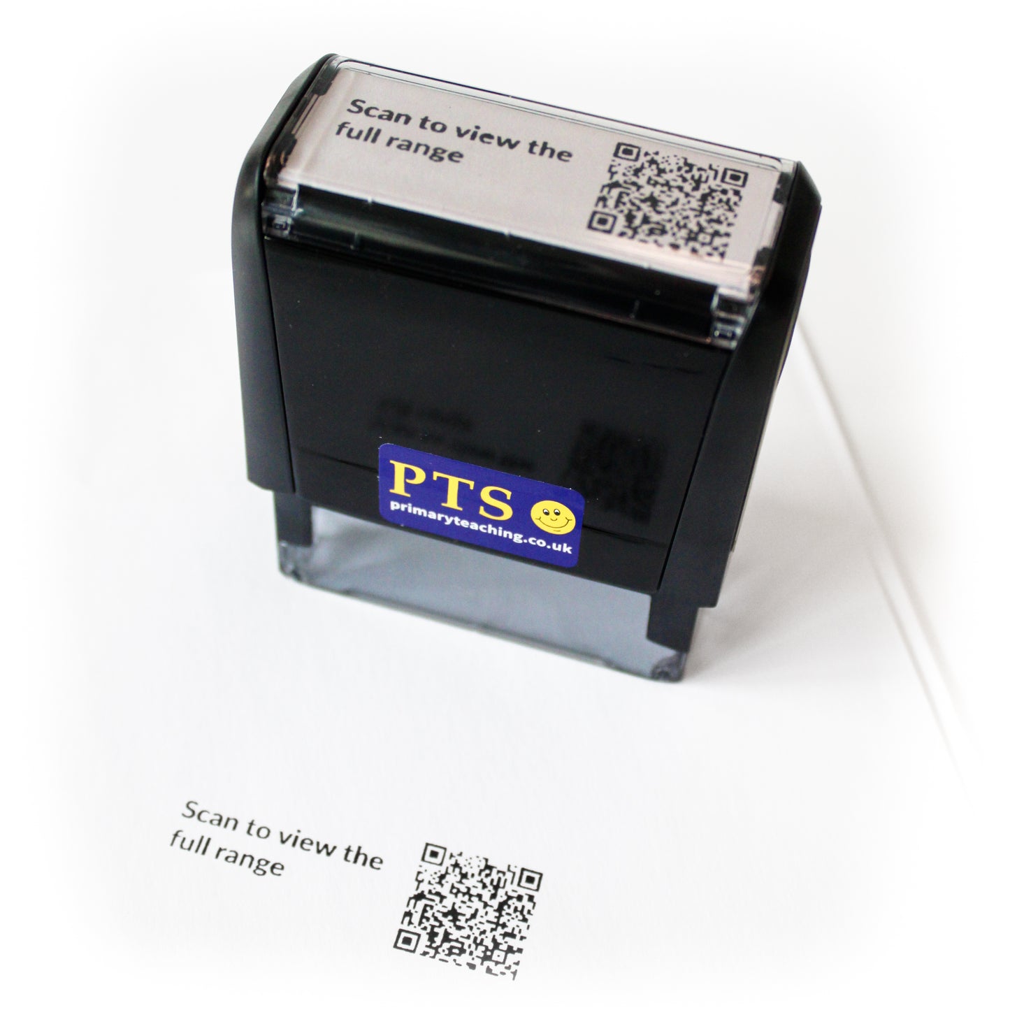 Custom QR code self-inking stamp shown stamping the text “Scan to view the full range” onto white paper.