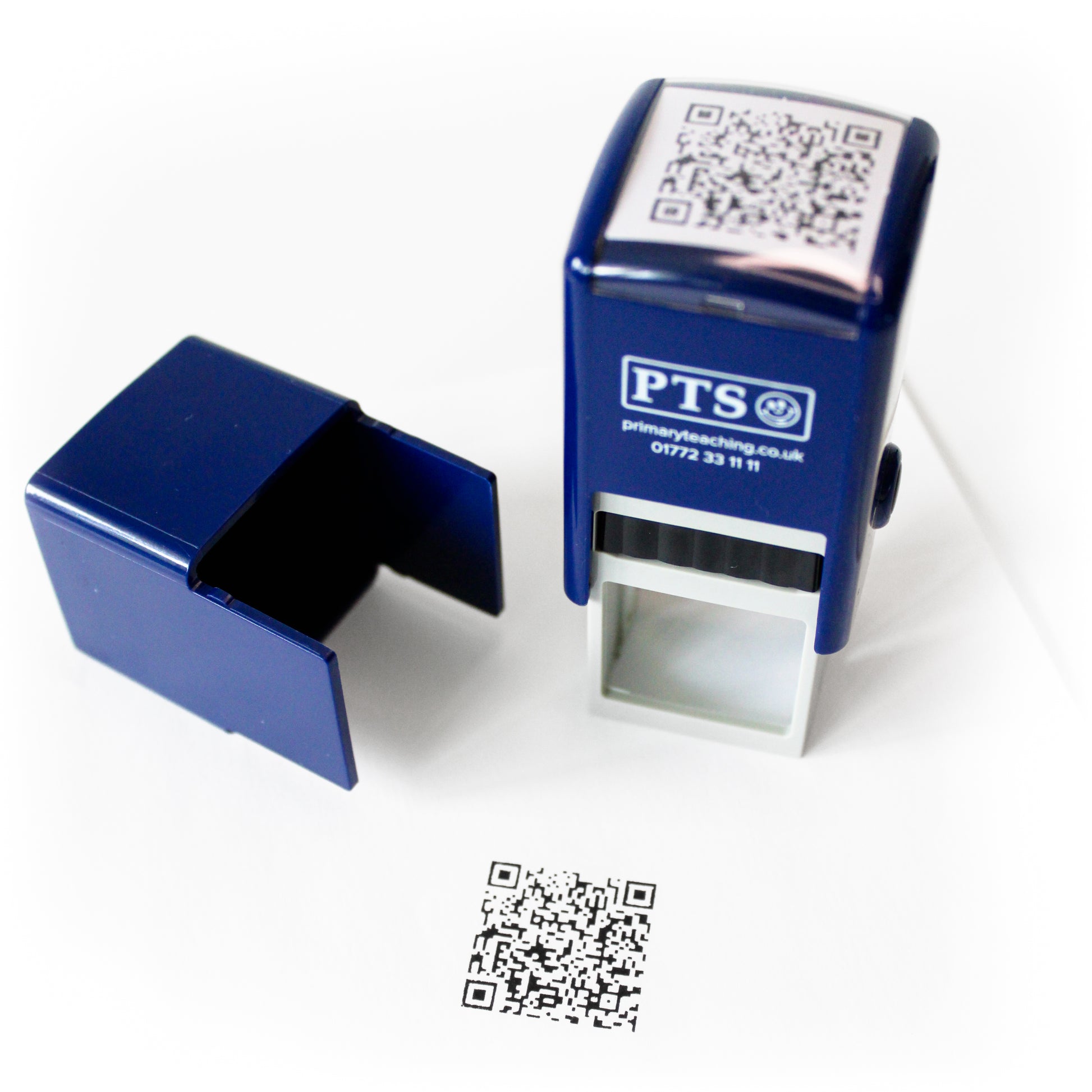 Black self-inking QR code stamp with protective cap removed, shown beside a stamped QR code impression on white paper.