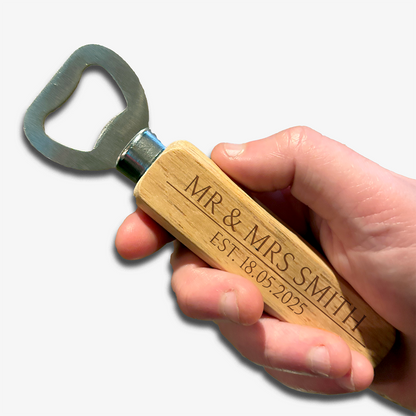 Hand holding bottle opener. Metal opener with wooden handle which has two rows of etched writing for you to personalised. Example text top: Mr & Mrs Smith, bottom: Est. 18.05.2025.