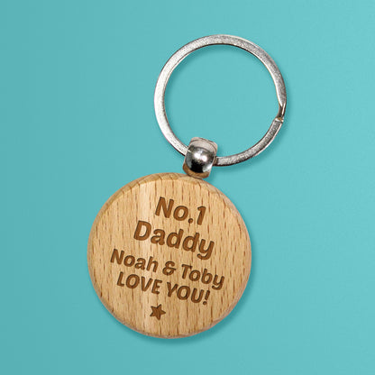 Circular wooden keyring with a metal ring, engraved with text for customisation saying 'No. 1 Daddy' and underneath 'Noah & Toby LOVE YOU!' with a star at the bottom.
