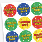 A sheet of 25mm round holographic 'Lunchtime Award' stickers. Each sticker features a vibrant, reflective background in colours such as red, blue, green, and yellow, with the text 'Lunchtime Award' in bold red or yellow letters. Ideal for recognising positive behaviour during lunchtime.
