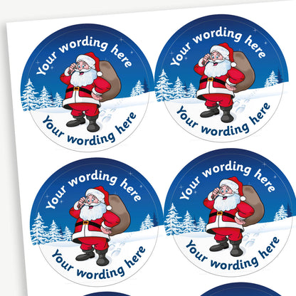A sheet of customisable circular stickers featuring a cheerful Father Christmas holding a sack of presents set against a snowy blue background with pine trees; includes customisable text above and below santa.