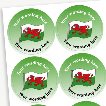 A sheet of customisable circular stickers featuring a green background with a central image of the Welsh flag.  Placeholder text 'Your Wording Here' arcs above the image for personalisation.