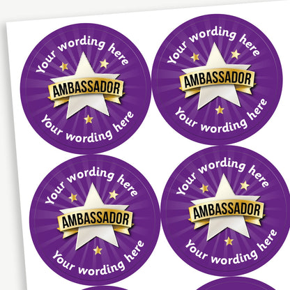 Sheet of round personalised stickers featuring a silver star design with a gold banner across is with the word 'AMBASSADOR' and stars on a purple, starburst effect, background; includes customisable white text above  and below the image.