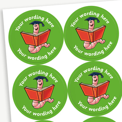 Sheet of round green stickers featuring a smiling cartoon bookworm wearing a graduation cap and holding an open red book. Each sticker includes placeholder text reading 'Your wording here' curved above and below the illustration. 
