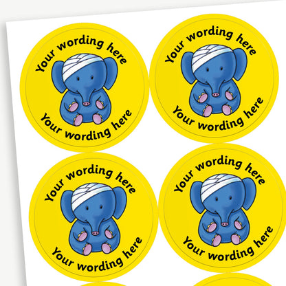 Sheet of round yellow stickers featuring an elephant with a bandage on it's head in the centre. Each sticker has placeholder text reading 'Your wording here' curved above and below the illustration. 