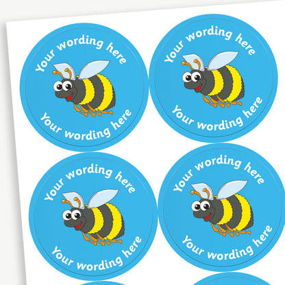 Sheet of round blue stickers featuring an cartoon bee in the centre. Each sticker has placeholder text reading 'Your wording here' curved above and below the illustration. 