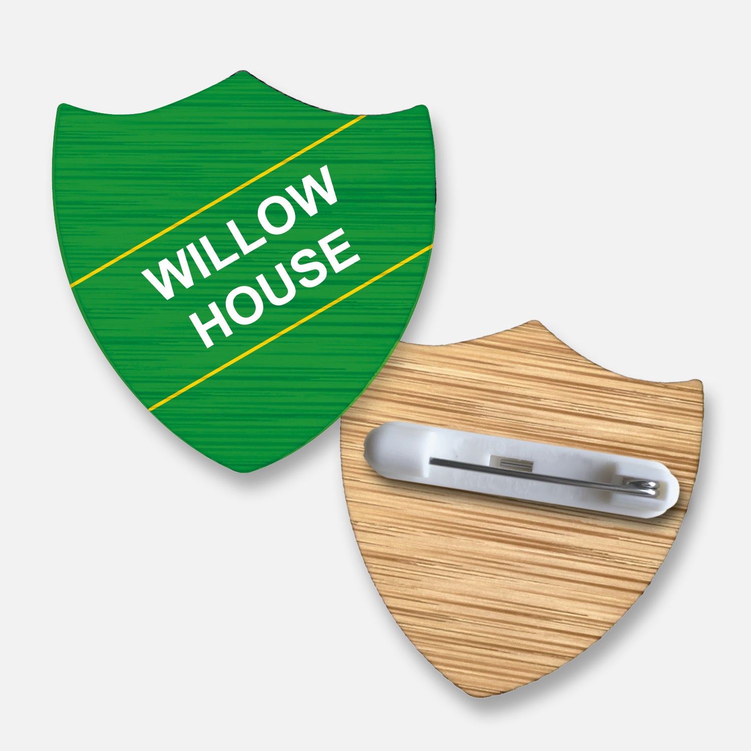 A 34mm x 36mm shield-shaped badge made from sustainable bamboo with a coloured or natural wood grain finish. The front displays two lines of customisable text printed diagonally in bold font with colour options. The reverse side is equipped with a secure metal pin fastening. This eco-friendly badge is ideal for recognising pupil roles, house affiliations, or achievements in educational settings.