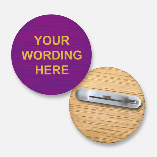 A 38mm circular badge crafted from natural bamboo coloured purple, featuring the placeholder text 'Your Wording Here' in yellow capital letters on the front, with a pin fastening on the reverse side.
