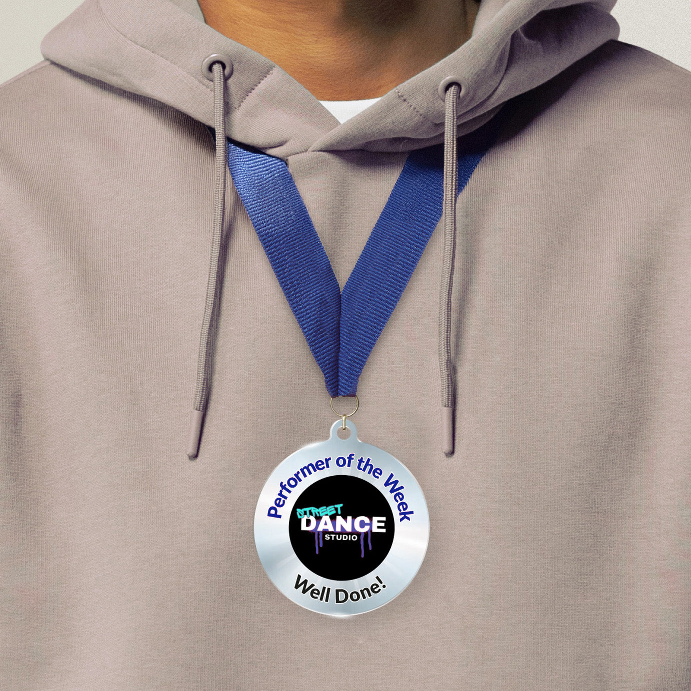 Acrylic personalised medal with blue ribbon showing silver design with 'Street Dance Studio image' and 'Performer of the Week', 'Well done!' wording. Medal worn around neck.
