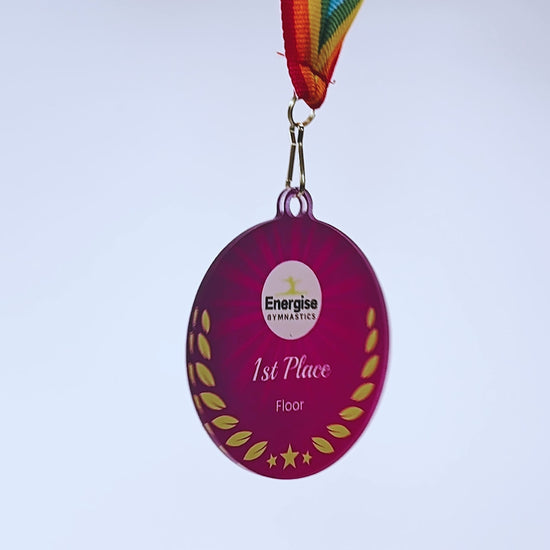 Video of a spinning purple acrylic medal with rainbow ribbon and personalised logo/text. The scene fades to a red acrylic medal with red/white/blue ribbon and personalised logo/text.