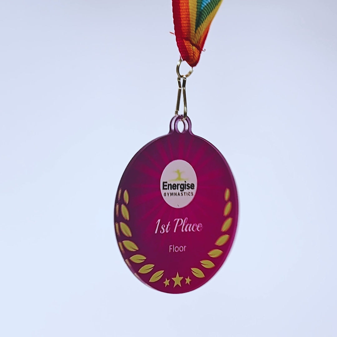 Video of a spinning purple acrylic medal with rainbow ribbon and personalised logo/text. The scene fades to a red acrylic medal with red/white/blue ribbon and personalised logo/text.