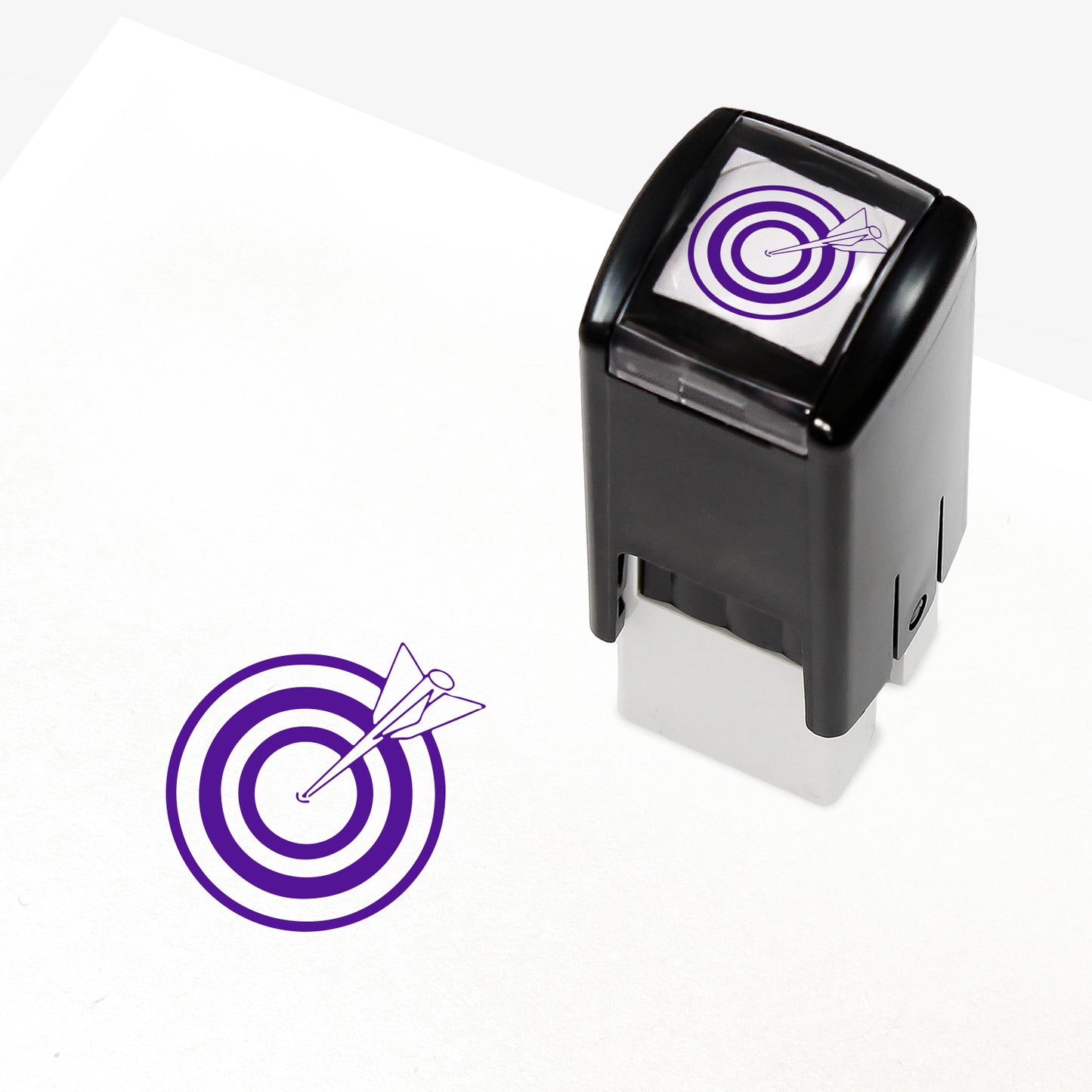 Target Stamper from Primary Teaching Services, featuring a compact black casing with a purple bullseye and arrow design. The stamp imprint measures 10mm in diameter and is available in various ink colours, ideal for marking pupil achievements.