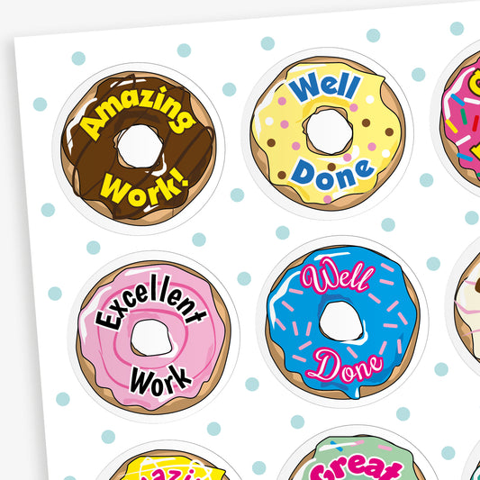 Sheet of 32mm vanilla-scented doughnut stickers in assorted pastel colours, each featuring phrases like 'Well Done', 'Great Work', and 'Brilliant Effort' in bold fonts; designed for rewarding pupils' achievements.