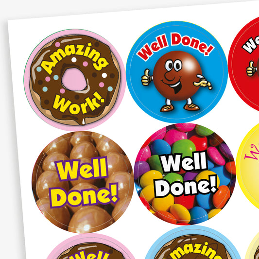 Sheet of 32mm chocolate-scented reward stickers featuring assorted colourful designs, including smiling chocolate characters, cupcakes, doughnuts, and sweets, each displaying motivational phrases like 'Well Done' and 'Amazing Work'; designed for rewarding pupils' achievements.